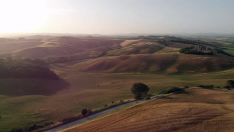 aerial-golden-hour-in-Tuscany,-drone-flying-backwards-above-typical-landscape