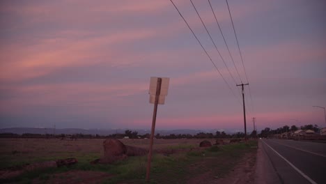 A-pastel-sky-over-the-Sierra-Nevada-mountains-with-power-lines-and-a-road-and-traffic-sign-in-the-foreground-in-Clovis,-CA,-USA