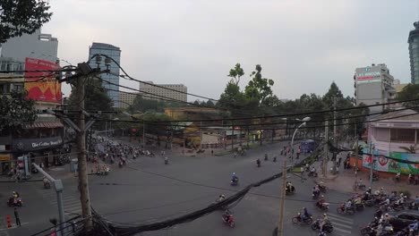 A-large-group-of-motorcyclists-and-cars-merge-through-each-other-at-a-intersection-in-Ho-Chi-Minh-City,-Vietnam