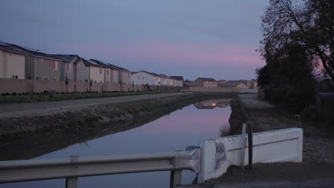 A-pastel-sky-over-a-canal-with-houses-in-the-background-in-Clovis,-CA,-USA