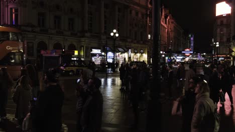 People-standing-looking-up-at-screen-piccadilly-circus-in-central-London-at-night