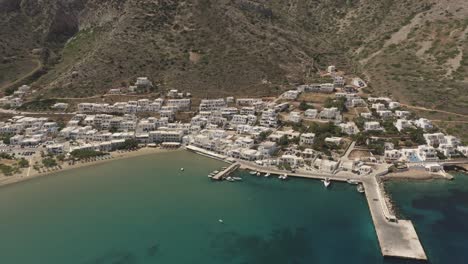 An-aerial-view-of-the-capital-city-and-port-of-the-island-of-Sifnos,-Kamares,-with-a-vibrant-cyan-blue-sea-and-traditional-white-houses