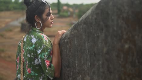 Young-lady-in-a-green-floral-print-shirt-and-white-pants-with-dark-hair-looking-at-a-farm-in-India
