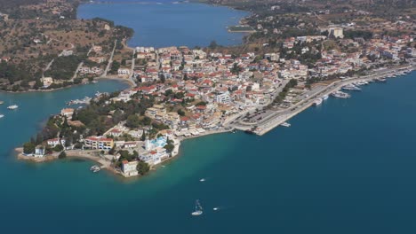 An-aerial-drone-view-of-Port-Cheli-in-Greece,-during-summer,-with-a-vibrant-blue-sea-and-several-sailboats-passing