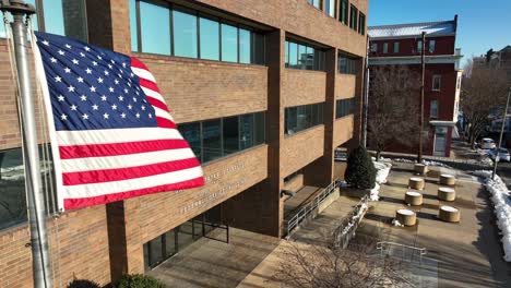 Aerial-view-of-American-flag-waving-in-front-of-Federal-Building-and-United-States-Courthouse-on-snowy-day