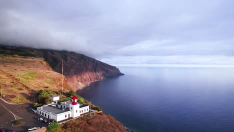Aerial-of-a-lighthouse-on-a-cliff-edge-on-rocky-volcanic-coast,-Madeira