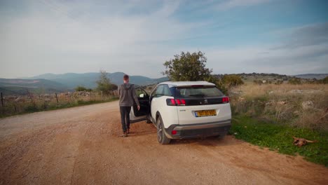 Man-exiting-car-on-dirt-road-with-rocky-terrain-and-walking-away-in-Kahal-Israel