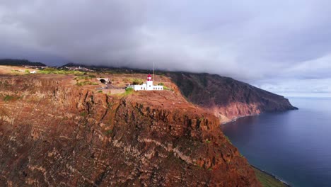 Aerial-view-of-a-lighthouse-on-top-of-a-volcanic-red-coastal-cliff,-Madeira