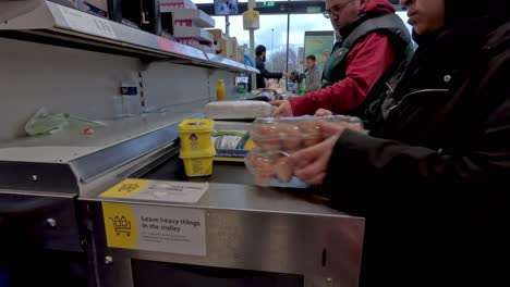 14-January-2023---Shopper-Placing-Eggs-And-Butter-Onto-Shopping-Conveyor-Belt-At-Checkout-At-Lidl-Supermarket