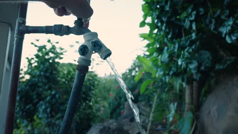 A-man's-hand-turning-on-a-stationary-outdoor-hose-with-water-slowly-starting-to-stream-out-in-slow-motion