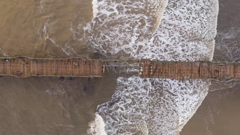 Capitola-pier-wreckage-from-bomb-cyclone-storm-destruction,-California,-Aerial-rising-Birdseye-view
