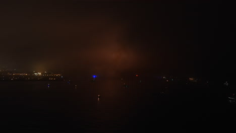 Lights-from-fireworks-glow-in-the-sky-on-a-foggy-Fourth-of-July---aerial-flyover