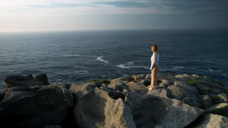 Young-Caucasian-Woman-Standing-On-The-Rock-While-Looking-In-The-Sea