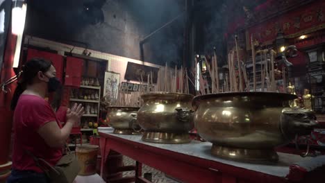 Asian-female-Praying-inside-a-Chinese-temple-in-Kuala-Lumpur,-Golden-Pots-with-burning-Incense-sticks