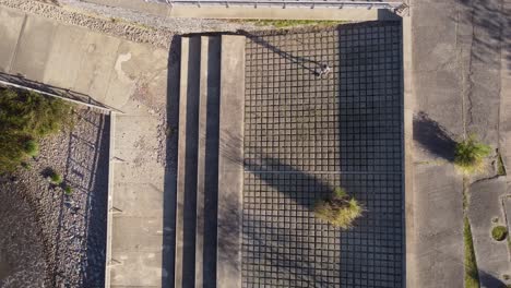 Luftaufnahme-Von-Oben-Nach-Unten-Eines-Mannes,-Der-Auf-Geometrischen-Formen-Auf-Dem-Boden-Am-Wasser-In-Buenos-Aires-Springt