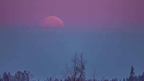 Time-lapse-of-pink-moon-descending-and-disappearing-behind-clouds-of-colorful-sky