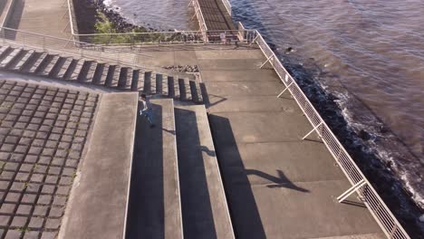 Young-man-jumps-on-steps-and-concrete-seafront-platform-with-geometric-shapes,-Buenos-Aires-waterfront,-Argentina