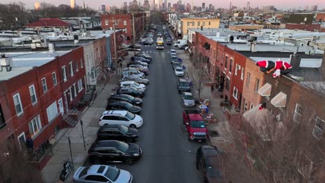 Aerial-tilt-up-reveal-of-bus-driving-down-crowded-city-street-surrounded-by-rowhouses-in-Philadelphia-suburb-neighborhood