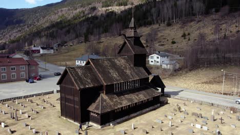 Aerial-view-of-a-person-walking-around-a-stave-church,-sunny-spring-day-in-Uvdal,-Norway