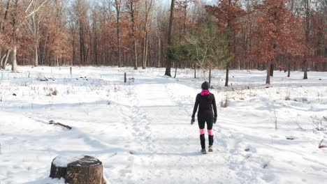 Woman-in-warm-exercise-clothing-walking-alone-on-snow-covered-forest-path