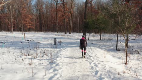 Woman-wearing-warm-exercise-clothing-walking-alone-on-winter-snowy-forest-path