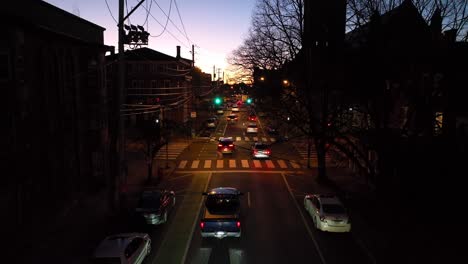 Slow-aerial-rising-shot-of-cars-driving-away-after-traffic-light-turns-green-at-night