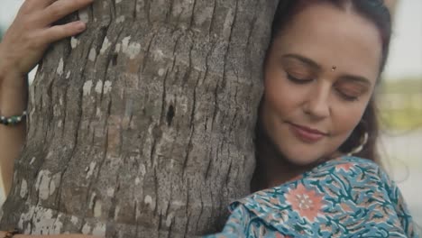 A-close-up-truck-pan-of-an-attractive-carefree-Caucasian-Female-holding-and-embracing-the-trunk-of-a-palm-tree