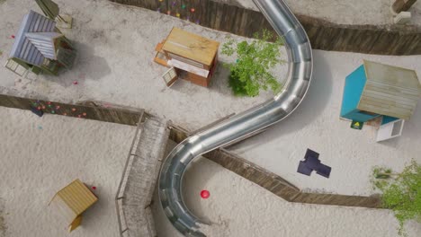 Aerial-flying-on-top-to-reveal-a-playground-with-children's-curved-slide-and-the-ground-lots-of-white-sand