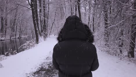 Walking-behind-female-in-winter-coat,-looking-over-her-shoulder-down-snowy-woodland-pathway
