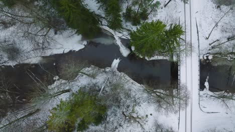 Aerial-establishing-view-of-Nordic-woodland-forest-covered-with-light-snow-and-a-dark-river-,-rural-bridge,-overcast-winter-day,-low-clouds,-drone-dolly-shot-moving-right
