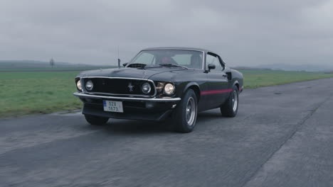 Ford-Mustang-Mach-1-Oldtimer-Bewegt-Sich-Auf-Nasser-Straße,-Klassischer-Amerikanischer-Sportwagen