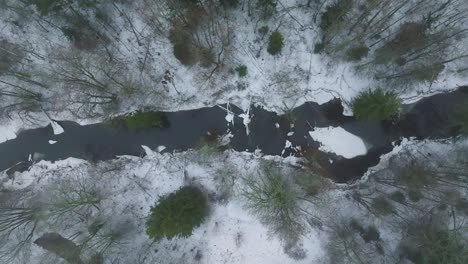 Aerial-establishing-view-of-Nordic-woodland-forest-covered-with-light-snow-and-a-dark-river-,-overcast-winter-day,-low-clouds,-birdseye-drone-dolly-shot-moving-left