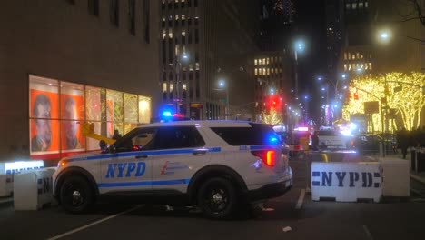 Las-Luces-De-La-Sirena-Del-Coche-De-Policía-De-La-Policía-De-Nueva-York-Parpadean-Estacionadas-Junto-A-La-Carretera-Con-Barreras-De-Hormigón-De-Seguridad-Por-La-Noche-En-La-Ciudad-De-Nueva-York,-EE.UU.