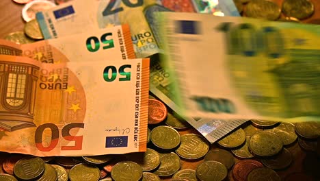 Un-Conjunto-Variado-De-Billetes-De-Euro-Revoloteando-Sobre-Una-Mesa-Cubierta-De-Monedas-De-Euro,-Primer-Plano