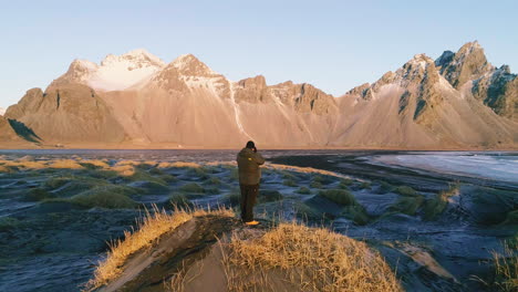 Fotógrafo-Capturando-La-Pintoresca-Montaña-Vestrahorn-De-Pie-En-La-Duna-De-La-Playa-De-Stokksnes