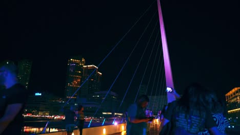 Grupo-De-Personas-Caminando-Y-Tomando-Fotos-En-El-Famoso-Puente-De-La-Mujer-Por-La-Noche-En-Buenos-Aires,-Argentina