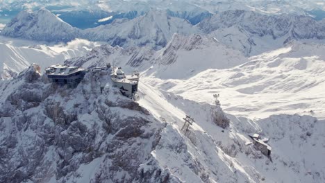 Antenne-Des-Gipfelgebäudes-Auf-Einem-Dramatischen-Berggipfel,-Der-Schneebedeckte-Berge-Im-Hintergrund-Enthüllt