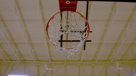 Looking-up-to-Basketball-hoop-against-School-gym-ceiling,-Ventilation-fans-spinning-in-Background