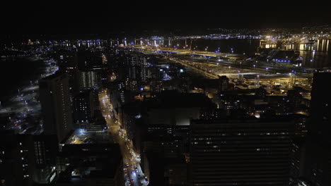 Dron-Lento-Aéreo-De-La-Ciudad-De-Durban-Por-La-Noche-Con-Las-Luces-Del-Puerto-En-El-Fondo