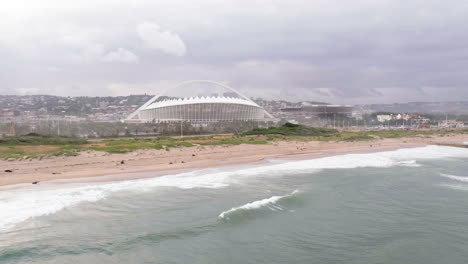 Luftdrohne-über-Dem-Indischen-Ozean-Mit-Dem-Fußballstadion-Moses-Mabhida-Im-Hintergrund-In-Südafrika
