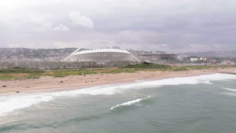 Drone-Aéreo-Sobre-El-Océano-índico-Con-El-Estadio-De-Fútbol-Moses-Mabhida-En-El-Fondo-En-Sudáfrica