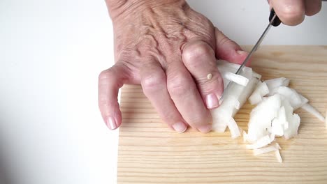 Caucasian-person-with-old-hands,-cutting-onion,-on-a-wooden-board