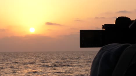 Silhouette-Des-Fotografen-Und-Ausklappbarer-Bildschirm-Und-Dslr-kamera,-Die-Den-Orangefarbenen-Sonnenuntergang-über-Dem-Ozean-Filmen