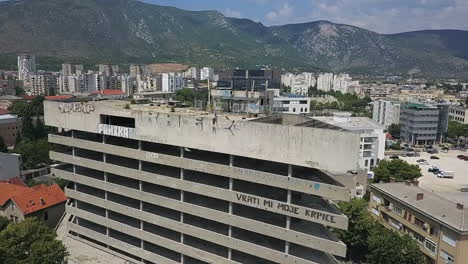 Aerial-orbits-multi-floor-abandoned-parkade-in-old-city,-Mostar-Bosnia