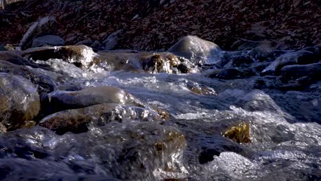 Toma-Estrecha-De-Un-Arroyo-De-Invierno-Mientras-El-Agua-Fluye-Sobre-Piedras-Cubiertas-De-Hielo