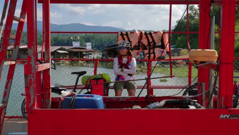 Shot-of-a-lonely-rider-sitting-along-lakeside-surrounded-by-hilly-terrain-in-Pak-Nai-fisherman-village,-Nan-province,-Thailand-at-daytime