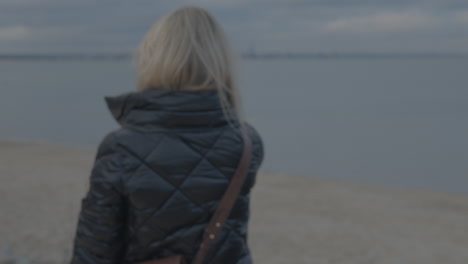 Blick-Von-Hinten-Frauen-Mit-Blonden-Haaren-Und-Schwarzer-Jacke-Halten-Telefon-Hoch,-Um-Am-Bewölkten-Tag-Am-Strand-In-Danzig-Ein-Foto-Zu-Machen