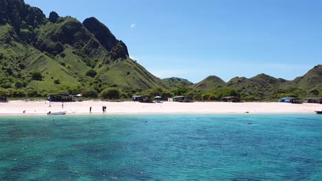 Tourist-walking-on-popular-Pink-Beach-with-sandy-coastline-and-crystal-clear-turquoise-ocean-water-within-Komodo-National-Park,-Indonesia