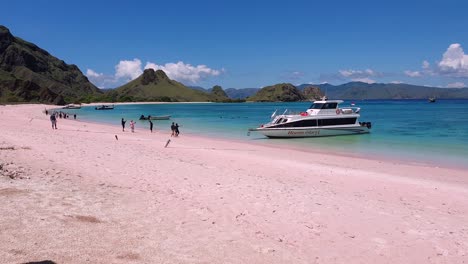 Tourist,-Der-Zeit-Auf-Rosa-Strand-Mit-Rosa-Sandstrandlandschaftsblicken,-Kristallklarem-Türkisfarbenem-Ozeanwasser-Und-Booten-Im-Komodo-Nationalpark-In-Indonesien-Genießt