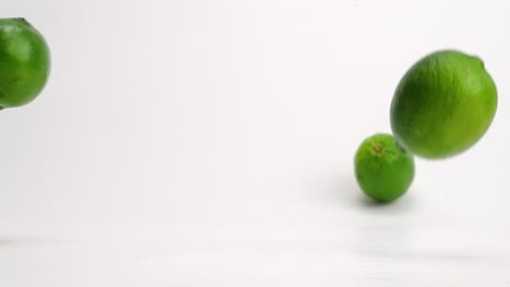 Bright-green-whole-limes-bouncing-in-slow-motion-onto-white-table-top